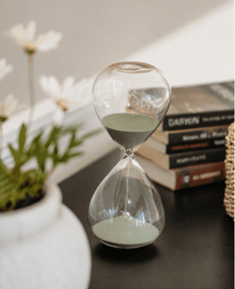 Reloj de arena junto a un florero con manzanilla y una pila de libros